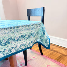 Load image into Gallery viewer, Tablecloth with light teal and blue floral block print pattern on a wooden chair in a room.