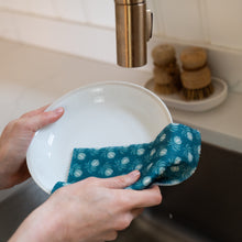 Load image into Gallery viewer, Person cleaning a white plate with a blue polka dot cloth in a kitchen sink.